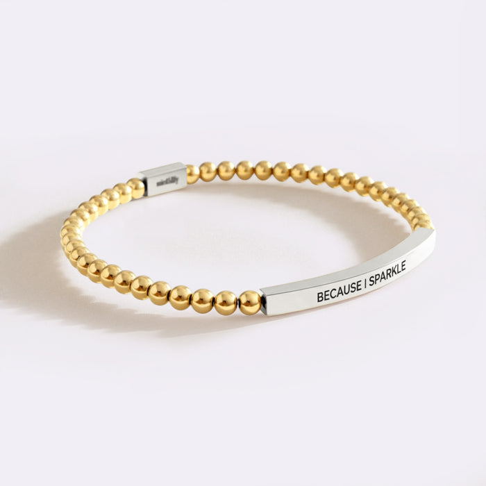Gold beaded bracelet with a silver tag on a white background
