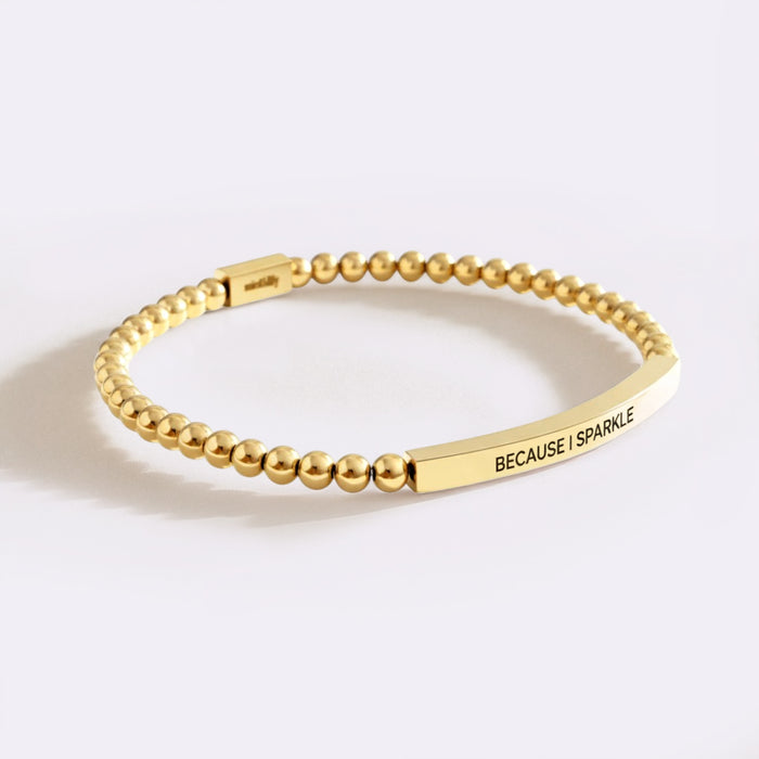 Gold beaded bracelet with a bar charm on a white background