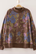 A brown long-sleeve sweatshirt with a large floral pattern in blue, pink, and olive green, hanging on a wooden hanger against a plain white wall.
