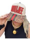 Person wearing a cap with 'BOUJEE' text and leopard print visor, holding it up.