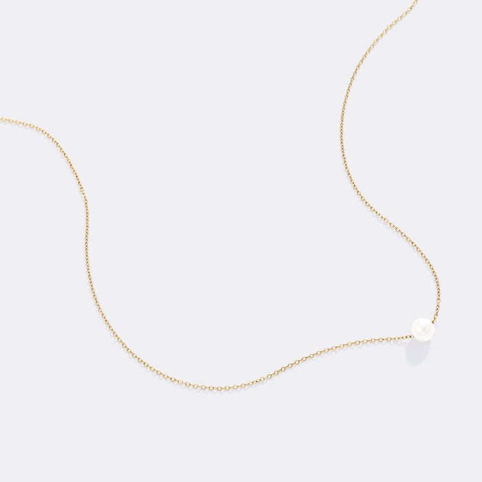 Gold necklace with a small white pendant on a light gray background