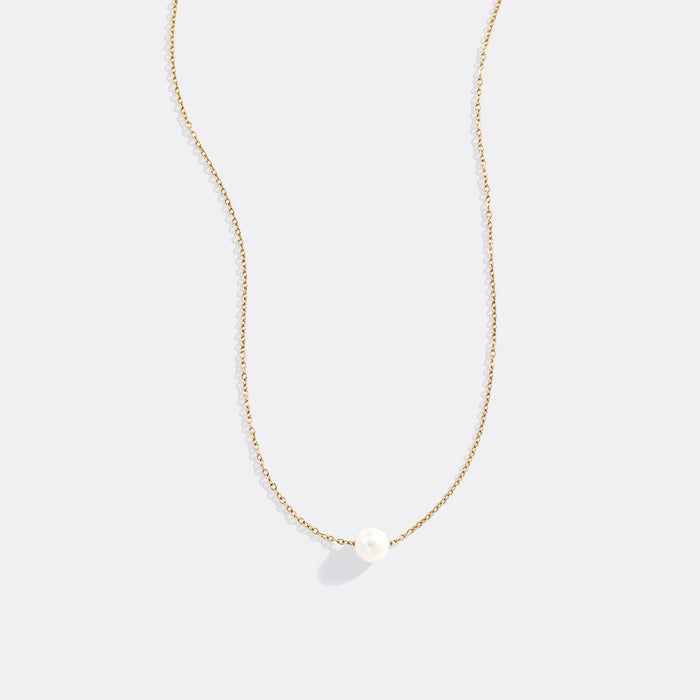 Gold necklace with a single pearl pendant on a light gray background