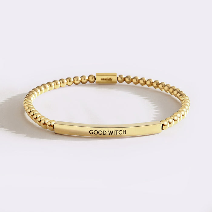 Gold bracelet with 'GOOD WITCH' engraving on a light background