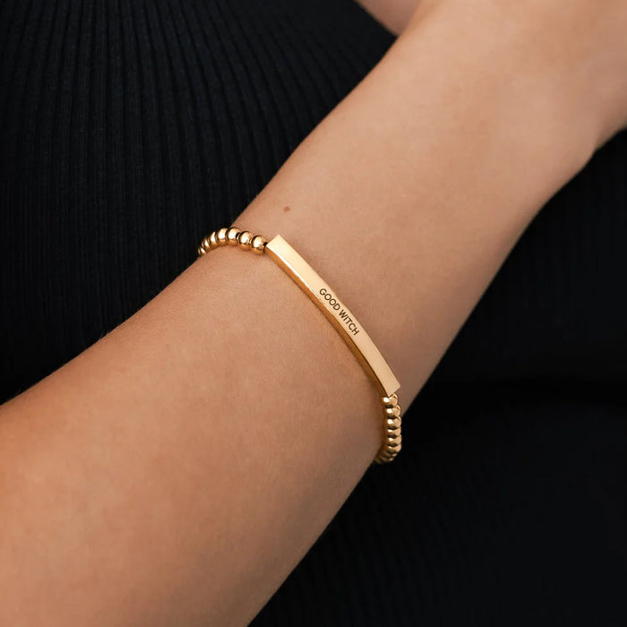 Gold bracelet with 'GOOD VIBES' engraving on a wrist against a black background