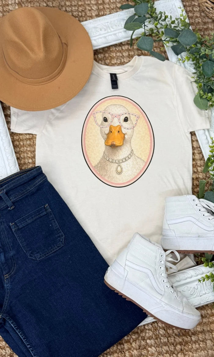 White t-shirt with a goose graphic, paired with a brown hat, blue jeans, and white sneakers on a textured surface.