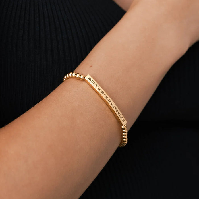 Gold bracelet with engraved text on a wrist against a black background