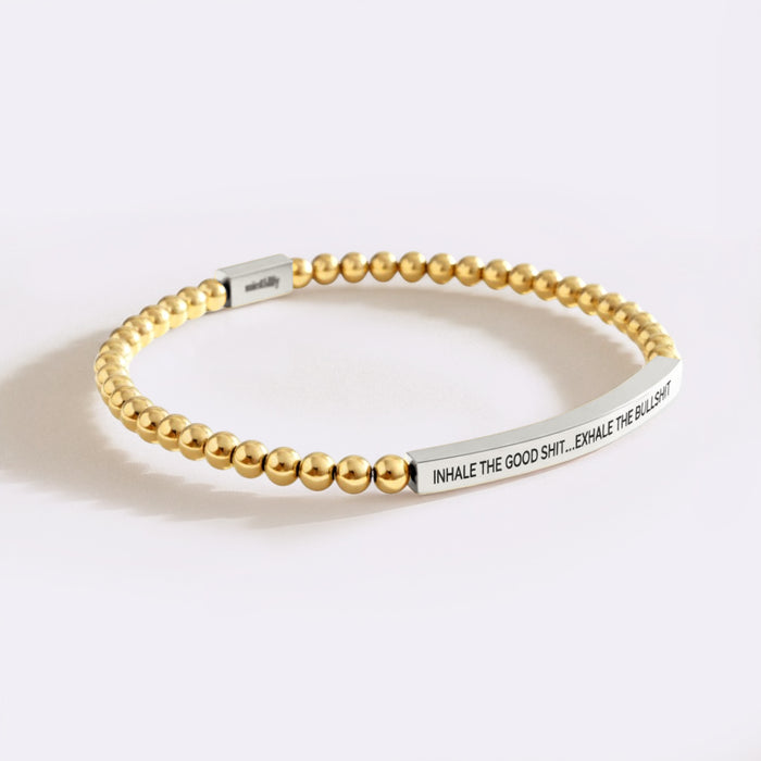 Gold beaded bracelet with silver tag on a white background