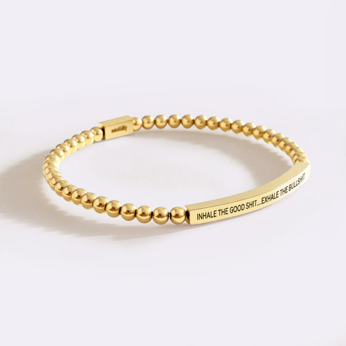 Gold beaded bracelet with motivational quote on a white background
