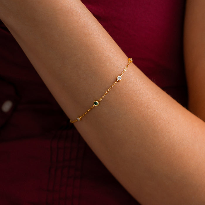 Gold bracelet with green gemstone on a wrist against a dark background