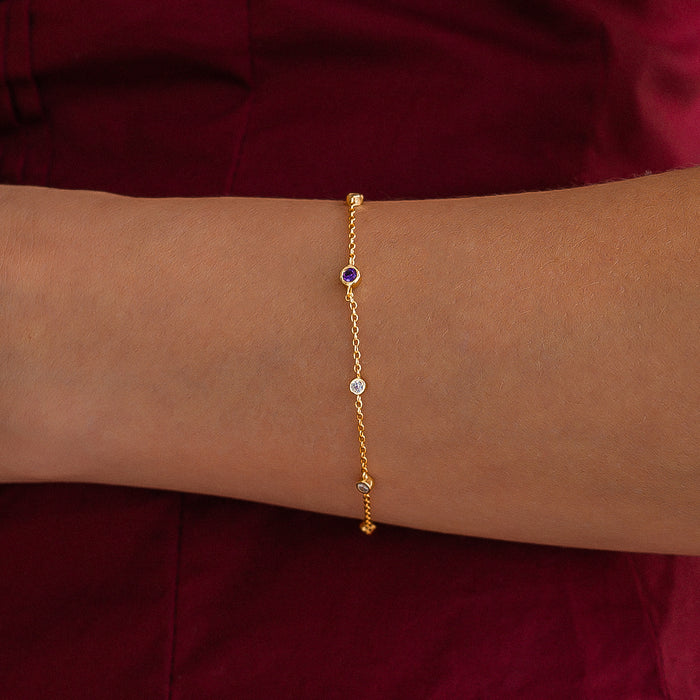 Gold bracelet with gemstones on a wrist against a maroon background