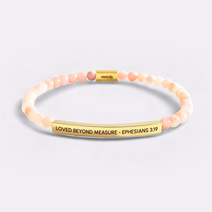 Bracelet with pink beads and gold bar with text on a light gray background