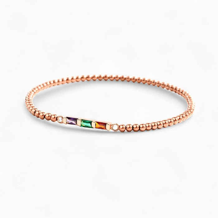 Rose gold bracelet with small beads and a central gemstone on a white background