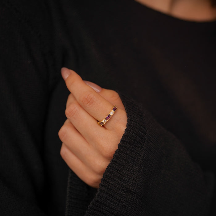 Hand wearing a gold ring with a purple gemstone against a dark background
