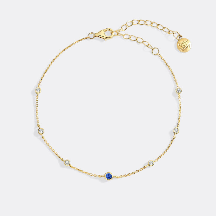 Gold bracelet with small gemstones on a light gray background