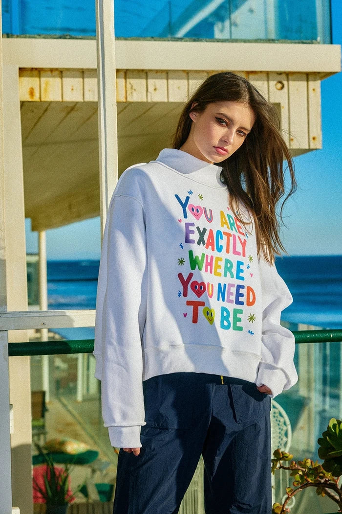 Person wearing a colorful sweatshirt with text by the beach